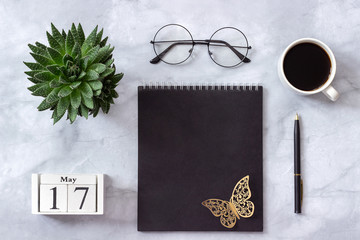 Office or home table desk. Wooden cubes calendar May 17. Black notepad, cup of coffee, succulent, glasses on marble background Concept stylish workplace Flat lay Top view