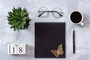 Office or home table desk. Wooden cubes calendar May 18. Black notepad, cup of coffee, succulent, glasses on marble background Concept stylish workplace Flat lay Top view