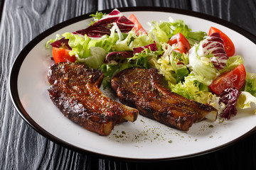 Serving fried lamb ribs with fresh vegetable salad close-up on a plate. horizontal