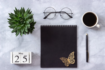 Office or home table desk. Wooden cubes calendar May 25. Black notepad, cup of coffee, succulent, glasses on marble background Concept stylish workplace Flat lay Top view