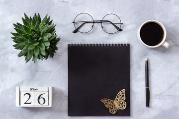 Office or home table desk. Wooden cubes calendar May 26. Black notepad, cup of coffee, succulent, glasses on marble background Concept stylish workplace Flat lay Top view
