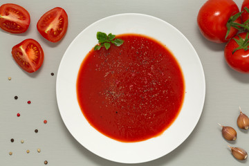 Tomato soup in a white bowl on grey background. Delicious soup of tomatoes and fresh herbs with garlic and spices. Top view.