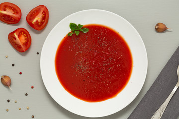 Tomato soup in a white bowl on grey background. Delicious soup of tomatoes and fresh herbs with garlic and spices. Top view.