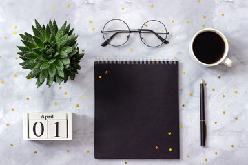 Office or home table desk. Wooden cubes calendar April 1st. Black notepad, cup of coffee, succulent, glasses on marble background Concept stylish workplace Flat lay Top view
