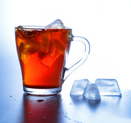 A glass cup with cold tea and ice cubes in it. Close-up. White-blue background. High contrast.