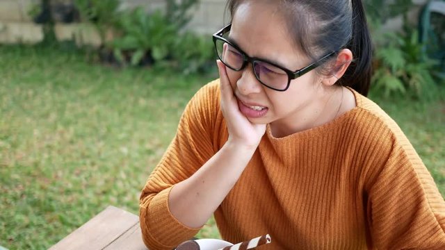 Closeup portrait with Asian young woman with hypersensitive teeth eating ice cream. Health and tooth Problem concept.