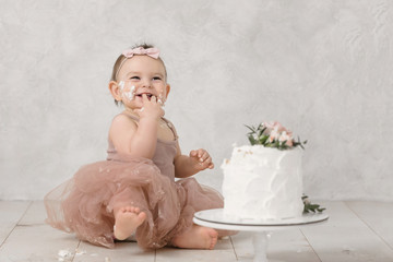 Portrait of a little cheerful birthday girl with the first cake. Eating the first cake. Smash cake