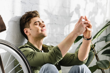 man in green shirt holding smartphone, sitting near brick wall, bicycle and plants  in office