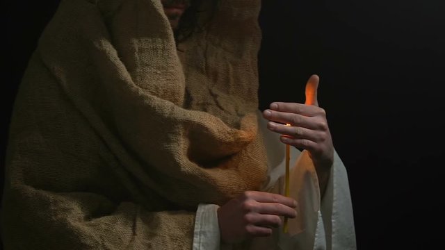 Parishioner in robe holding burning candle, praying God, asking for help