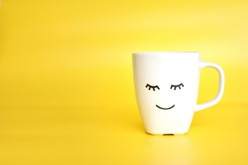 White tea or coffee cup with cute closed eyes face, good morning, day start concept, place for text.