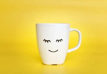 Good morning concept, white coffee cup with cute smiley face on bright yellow background.