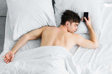 Fototapeta na wymiar handsome man sleeping under blanket near smartphone with blank screen on bad