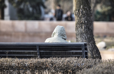 man in the hood sits on a bench