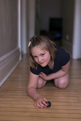 Vertical shot of beautiful little girl crouched on corridor hardwood floor playing with large glass marble in soft focus and looking up with mischievous look