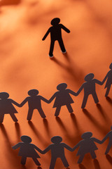 Paper human figure standing in front of paper people holding hands on red surface. Bulling,...