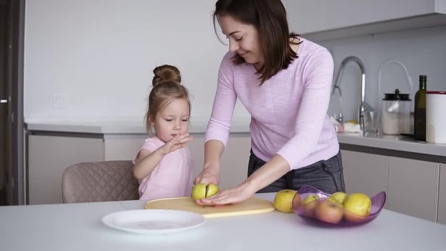 Mom and daughters cooking healthy food at home and having fun. Young woman cutting yellow apple on the desk in front her daughter. Household, teamwork helping, maternity concept