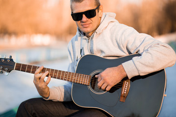 Obraz premium Young man sitting on steps playing guitar and singing, music concept