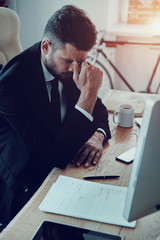 Exhaustion. Tired young man in formalwear massaging nose while sitting in the office