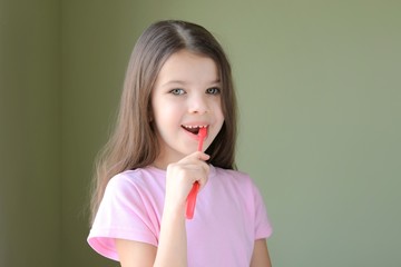 Girl brushing her teeth. Long haired smiling beautiful caucasian white girl brushing teeth with pink toothbrush on green background. Green eyed cute child in pink tshirt doing her morning hygiene. 