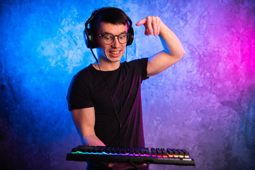 Close-up on gamer's hands going to press a key on a keyboard. Background is lit with neon lights