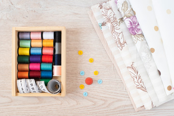 Composition with sewing threads, fabrics and accessories on wooden background, top view