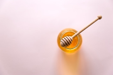 Honey pot and wooden dipper on pink background. Top view. Copy space. Selective focus