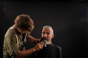 barber cuts a beard to a client to an elderly gray-haired man