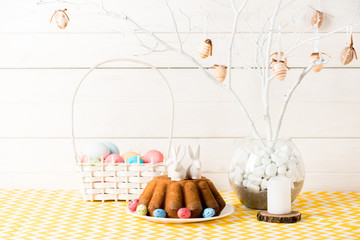 Easter cake with ceramic bunnies and wicker basket with painted eggs on table on wooden