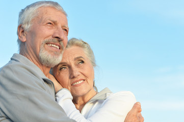 Portrait of happy senior couple hugging against blue sky