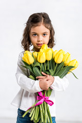 Front view of cute curly kid holding tulips bouquet on white