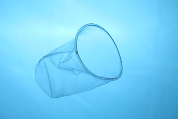 Plastic cup in blue water, plastic pollution of oceans.