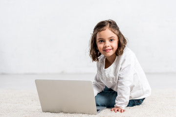 Concentrated brunette kid looking down while using laptop on white