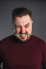Designer or artist, ready to work and holds a pencil in his teeth. Man with a beard in casual clothes posing on an isolated dark background, wearing a burgundy sweater in a studio