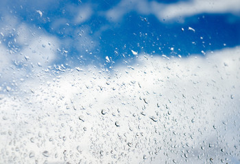 Drops of rain on the  transparent window glass  against cloudy blue sky ,  during rainy season.