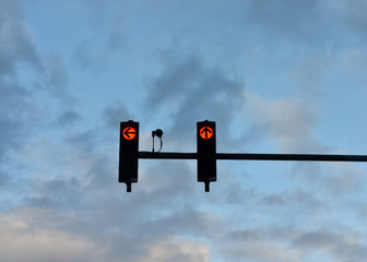 Low angle view of red  traffic lights   with the arrow pointing to ahead  and the left against cloudy blue  sky .