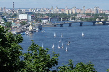 Fototapeta na wymiar View of Dnieper river, sailboats floating on water, right side of the Dnieper river riverside, buildings , bridge and river port. Kiev,Ukraine