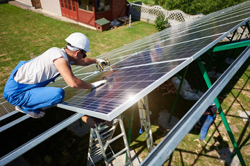 Professional worker installing solar panels on the green metal construction, using different equipment, wearing helmet. Innovative solution for energy solving. Use renewable resources. Green energy.