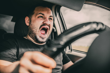 A young man driving a car in shock screams in fear of an accident