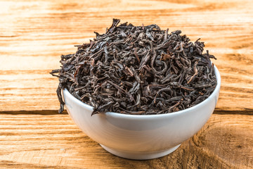 Dried tea is poured into a ceramic cup on a wooden plank table.