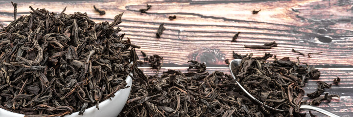 Dried tea is poured into a ceramic cup on a wooden plank table.