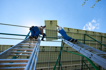 Professional workers team installing solar panels on the green metal construction using different equipment. Innovative solution for energy solving. Use renewable resources. Green energy.