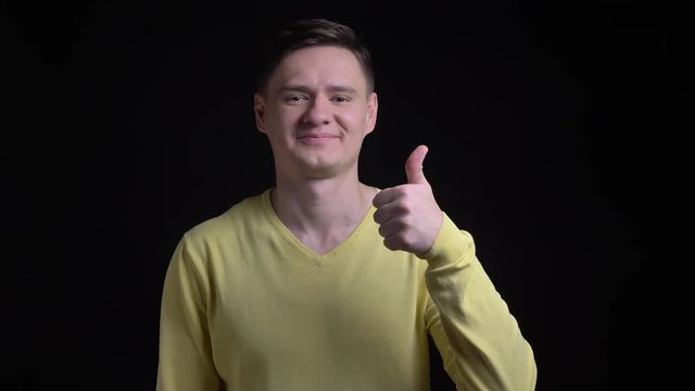 Middle-aged caucasian man in yellow sweater gesturing finger-up sign to show like and respect into camera on black background.