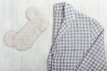 Grey pajamas and fluffy sleep mask on white wooden backgraund with copy space. Top view.