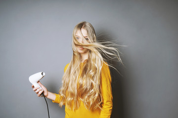 funny young blond woman blow-drying her long hair with blow dryer