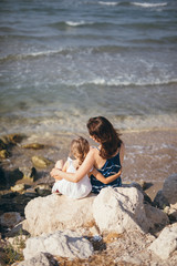Mother and daughter sitting on a stone near the sea embracing each other