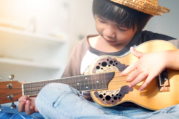 Happy smiling kid learning to play the ukulele guitar on bedroom