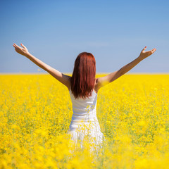 Naklejka na ściany i meble People freedom success concept. Happy woman in the field with flowers at sunny day in the countryside. Nature beauty background, blue sky and yellow flowers. Outdoor lifestyle.