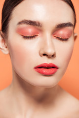 beautiful trendy young woman with glitter makeup and eyes closed isolated on coral