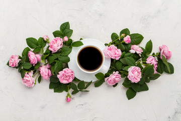 White cup with black coffee and pink roses on a light stone background. Flat lay, top view