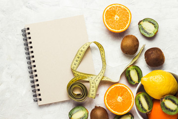 Notebook for entries, Measuring tape and Organic Fruits on a light stone background